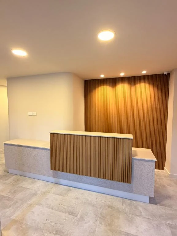 Recepción del consultorio con mueble en listones de madera y luz cálida
